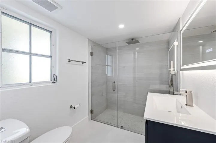 Modern bathroom featuring a frameless glass shower enclosure, a rain shower head, and light-toned wall tiling
