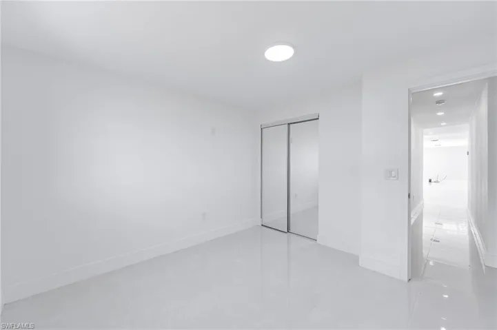 Bright room featuring white walls, glossy tile flooring, a circular ceiling light fixture, and mirrored sliding closet doors