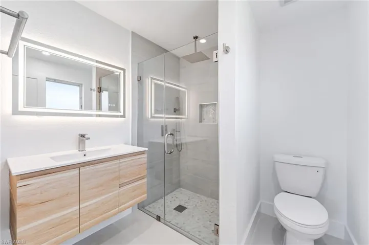 Modern bathroom featuring a floating wood-finish vanity with an integrated sink, a backlit mirror, and a glass-enclosed shower with a rain showerhead