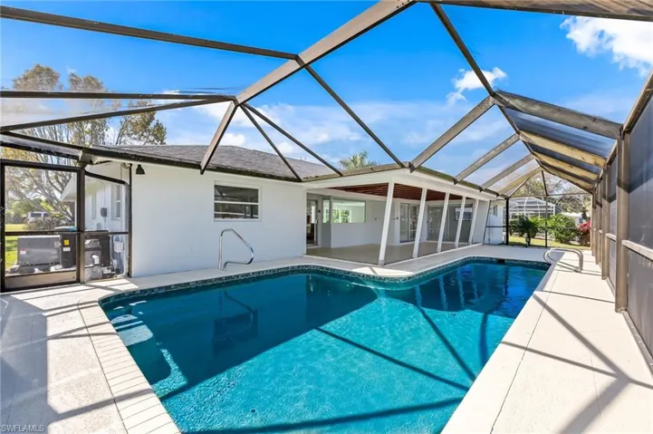 Screened-in outdoor pool featuring a paved deck, white stucco exterior, and a covered lanai with multiple sliding glass doors