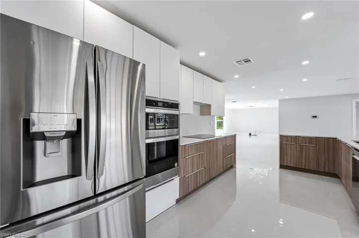 Modern kitchen featuring stainless steel appliances, dual-tone cabinetry, light countertops, and polished tile flooring