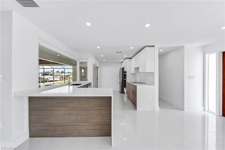 Open-concept kitchen featuring a peninsula with countertop seating, white cabinetry, dark wood-finish base cabinetry, stainless steel appliances, and a window overlooking a waterway