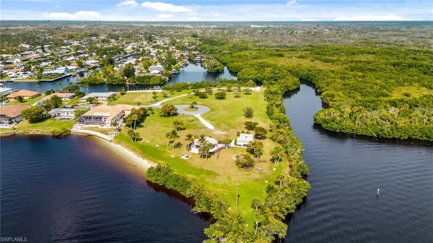 Expansive waterfront property featuring a substantial land parcel, mature tropical foliage, a private sandy shoreline, and direct water access