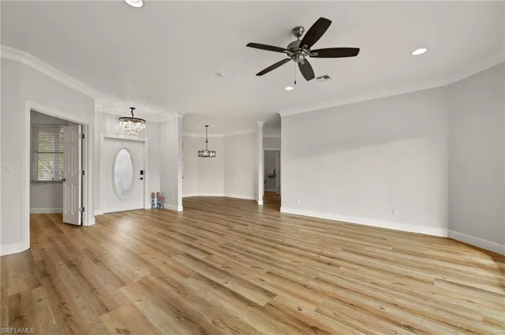 Unfurnished living room, formal dinning room and den on the left, light wood-style flooring, ornamental molding, ceiling fan, a chandelier, and recessed lighting
