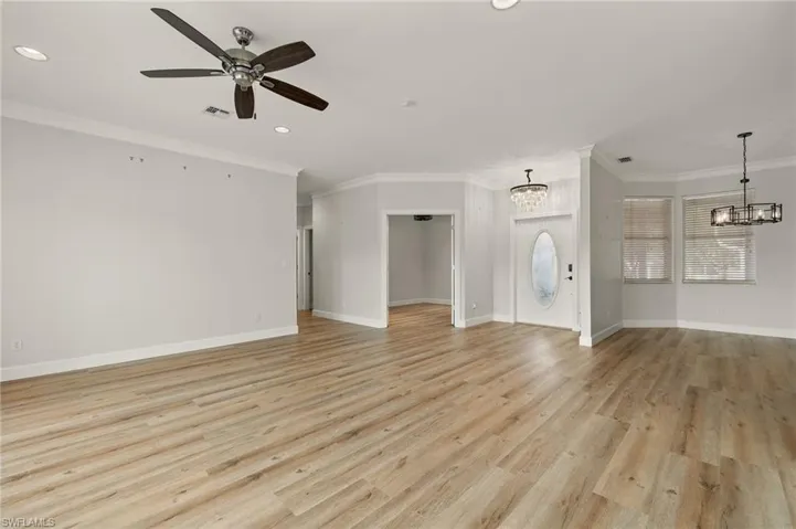 Unfurnished living room with the den on the left, featuring ornamental molding, light wood finished floors, a ceiling fan, a chandelier, and recessed lighting