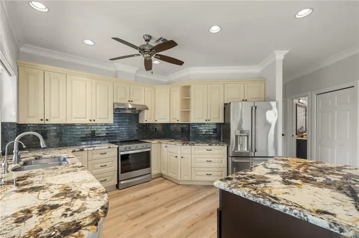 Kitchen with light stone counters, ornamental molding, stainless steel appliances, cream cabinets, and light wood finished floors
