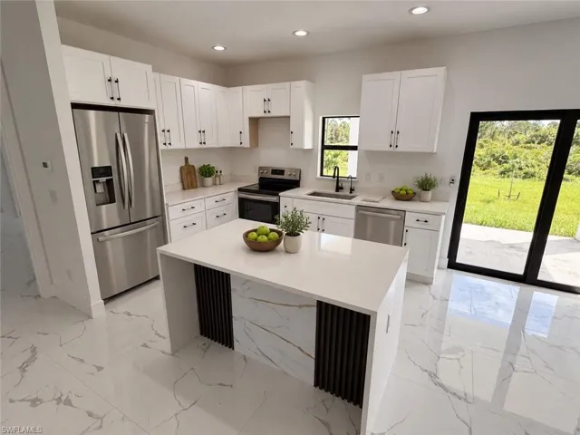 White shaker-style cabinetry with matte black hardware, stainless steel appliances, a center island with a waterfall countertop, white patterned tile flooring, and a large sliding glass door