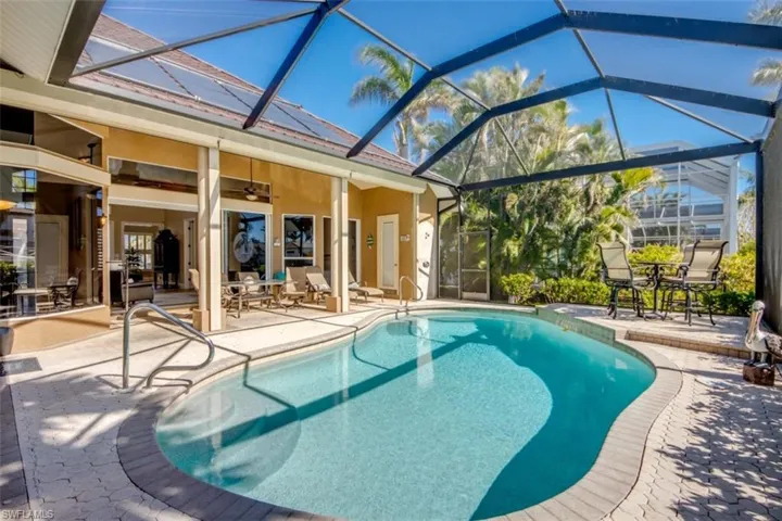 View of pool with glass enclosure, ceiling fan, and a patio area