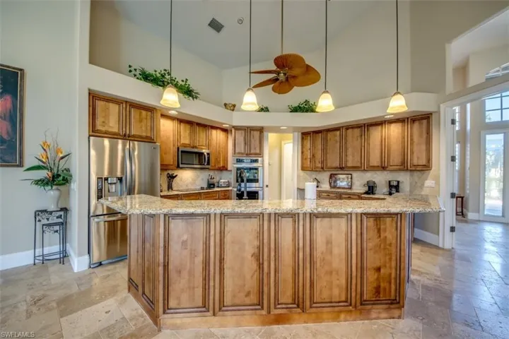 Kitchen featuring light stone countertops, appliances with stainless steel finishes, a center island, and high vaulted ceiling