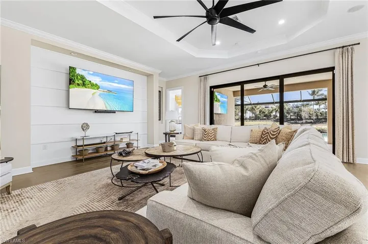 Living area with ceiling fan, wood finished floors, a raised ceiling, crown molding, and recessed lighting