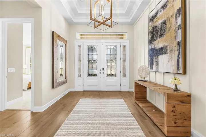Entryway with light wood-type flooring, hanging lights, french doors, ornamental molding, and a raised ceiling