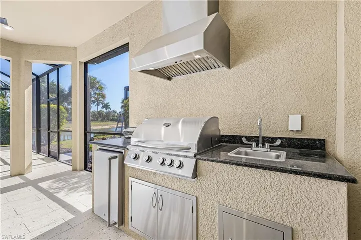 View of patio / terrace featuring a sunroom, glass enclosure, exterior kitchen, and a water view
