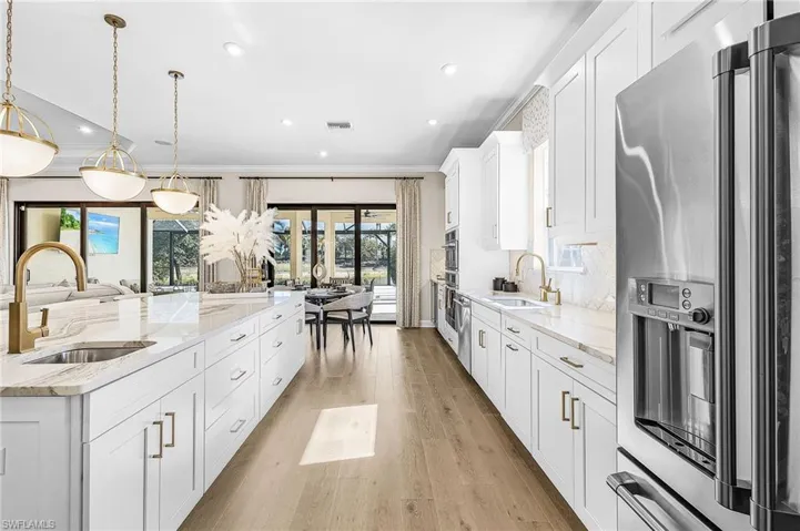 Kitchen with stainless steel fridge with ice dispenser, white cabinetry, light stone counters, light wood-type flooring, and decorative light fixtures
