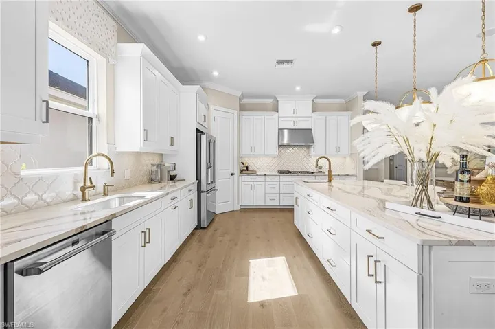 Kitchen featuring light stone countertops, stainless steel appliances, white cabinets, light wood finished floors, and hanging light fixtures
