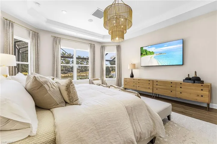 Bedroom featuring wood finished floors, a raised ceiling, ornamental molding, and a chandelier