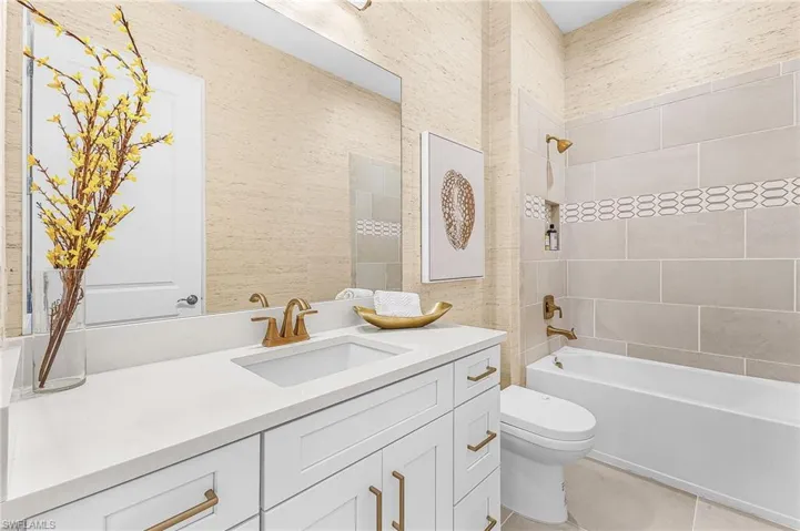 Bathroom with washtub / shower combination, vanity, wallpapered walls, and light tile patterned flooring