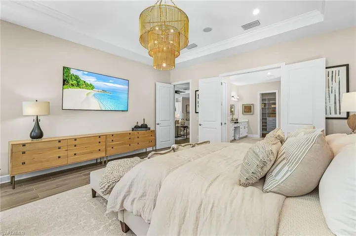 Bedroom with wood finish floors, hanging lights, crown molding, and ensuite bathroom