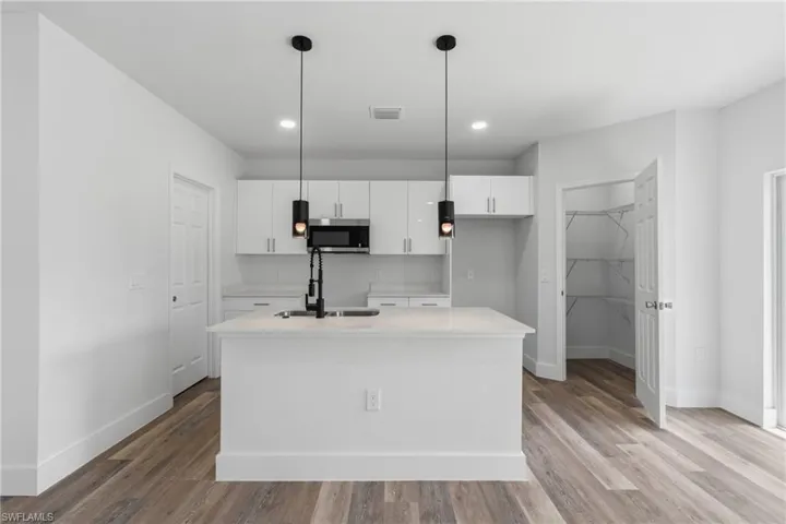 Kitchen with an island with sink, light stone countertops, white cabinetry, stainless steel microwave, and hanging light fixtures