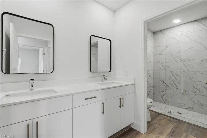 Full bathroom featuring double vanity, a marble finish shower, and dark wood-type flooring