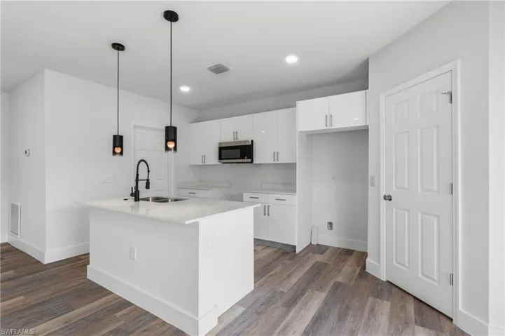 Kitchen with white cabinets, a center island with sink, stainless steel microwave, and dark wood-type flooring