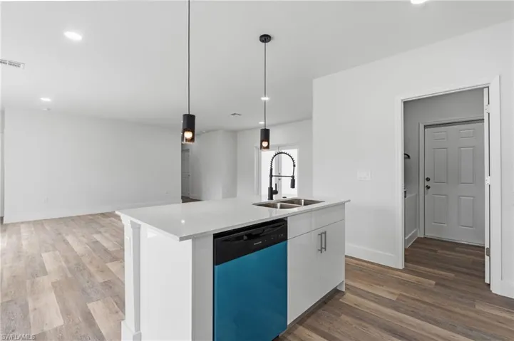 Kitchen with dishwasher, white cabinets, light stone countertops, dark wood-style floors, and a center island with sink