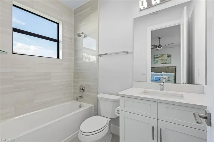 Full bathroom featuring vanity, toilet, tiled shower / bath combo, and ceiling fan