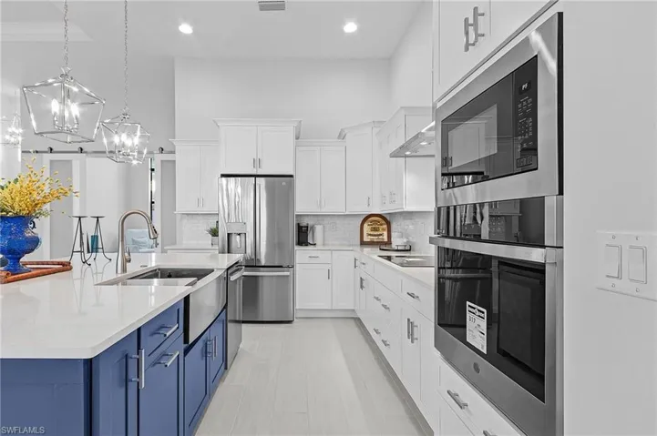 Kitchen featuring tasteful backsplash, blue cabinets, stainless steel appliances, decorative light fixtures, and white cabinets