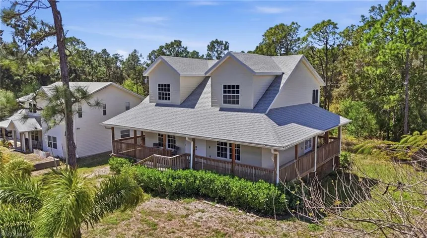 Country-style home featuring covered porch, a shingled roof, and view of wooded area