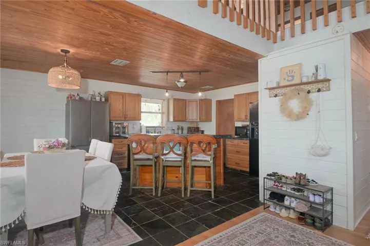 Kitchen featuring black appliances, track lighting, a breakfast bar area, wooden ceiling, and dark stone counters