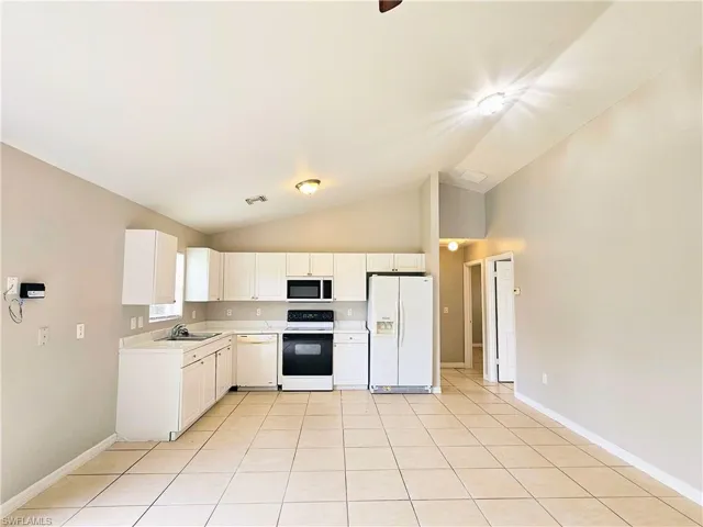 Kitchen with white appliances, light countertops, white cabinets, light tile patterned floors, and high vaulted ceiling