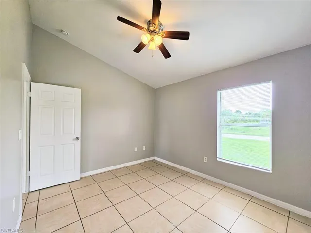 Empty room featuring lofted ceiling, light tile patterned floors, and a ceiling fan
