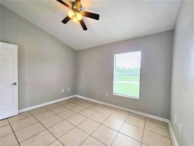 Empty room with light tile patterned flooring, vaulted ceiling, and a ceiling fan