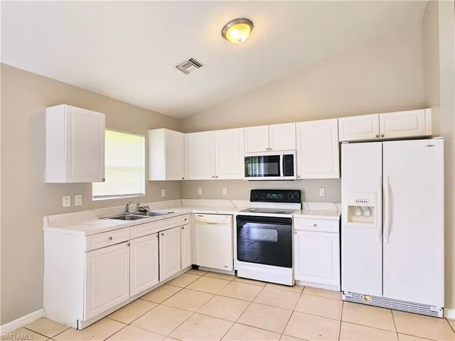 Kitchen with white appliances, vaulted ceiling, white cabinetry, light tile patterned flooring, and light countertops