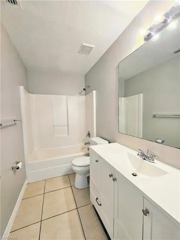 Full bath with bathing tub / shower combination, vanity, light tile patterned floors, and a textured ceiling