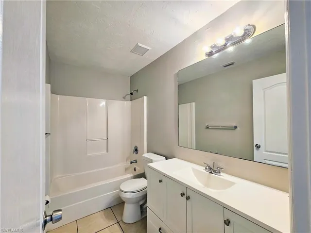 Bathroom featuring shower / bath combination, vanity, light tile patterned floors, and a textured ceiling