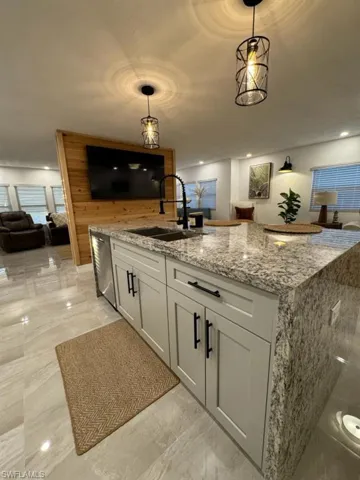 Kitchen with light stone countertops, stainless steel dishwasher, light tile flooring, hanging light fixtures, and sink