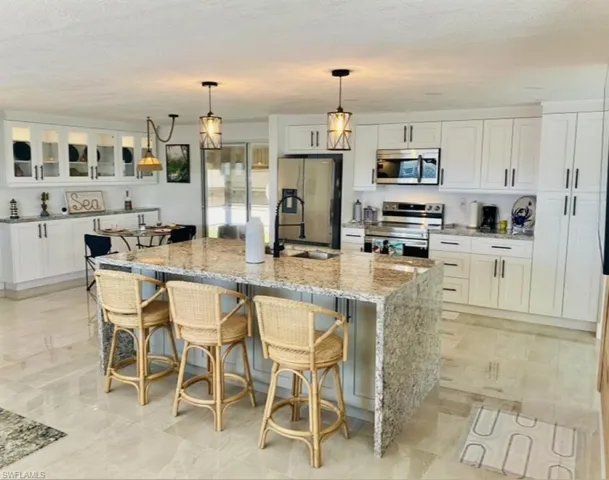 Kitchen featuring stainless steel appliances, white cabinetry, light tile flooring, and a kitchen island with sink