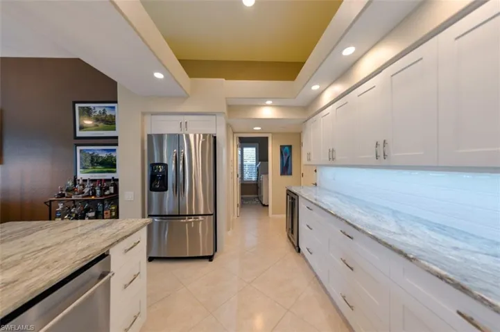 Kitchen featuring white cabinets, appliances with stainless steel finishes, light stone countertops, and light tile floors