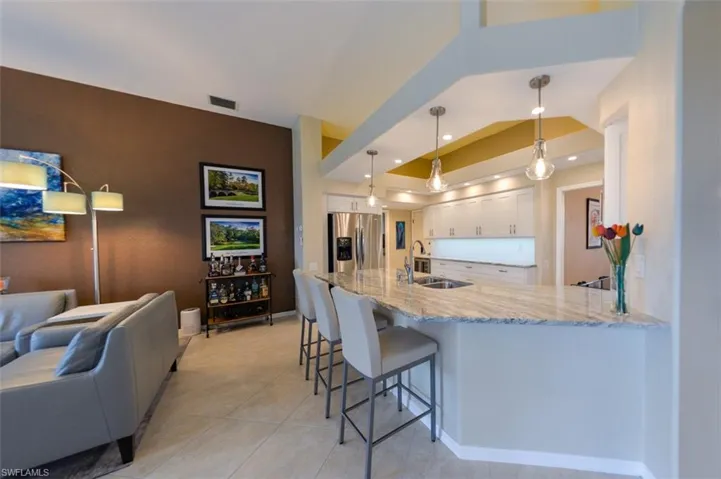 Kitchen featuring white cabinetry, stainless steel fridge, light stone counters, decorative light fixtures, and sink