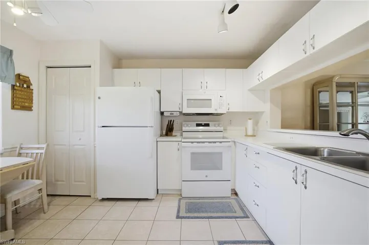 Kitchen featuring white appliances, light countertops, white cabinetry, and light tile patterned flooring