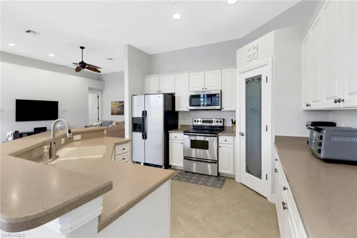 Kitchen with white cabinets, a center island with sink, ceiling fan, sink, and stainless steel appliances