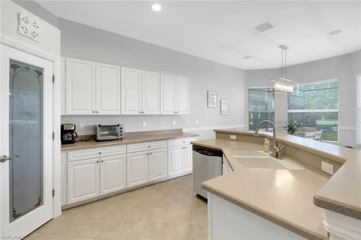 Kitchen featuring sink, decorative light fixtures, stainless steel dishwasher, white cabinets, and a chandelier