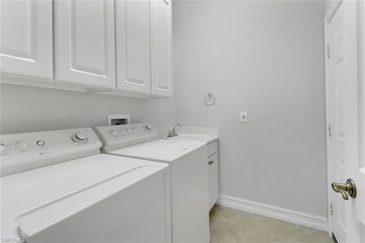 Laundry area with cabinets, sink, separate washer and dryer, and light tile patterned floors