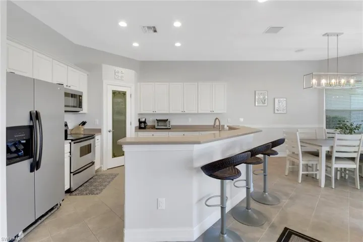 Kitchen with white cabinets, light tile patterned floors, a kitchen island with sink, decorative light fixtures, and stainless steel appliances