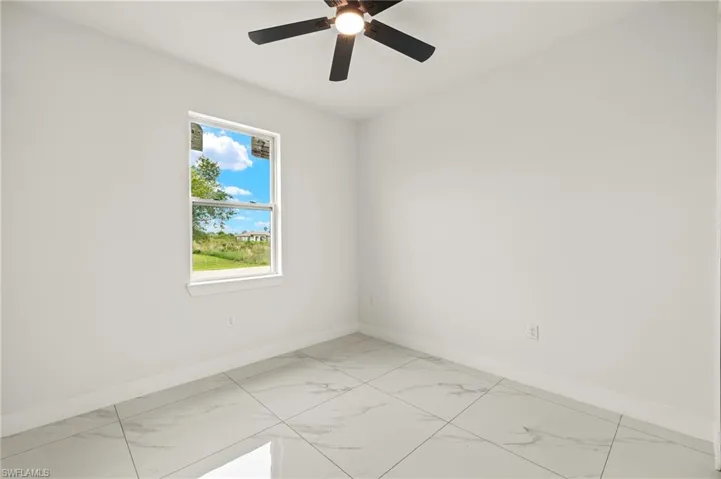 Spare room featuring baseboards, light marble finish flooring, and ceiling fan