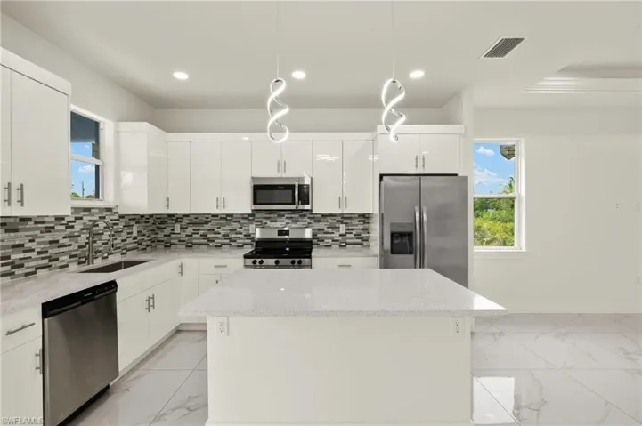 Kitchen featuring stainless steel appliances, light marble finish floors, a center island, a sink, and recessed lighting