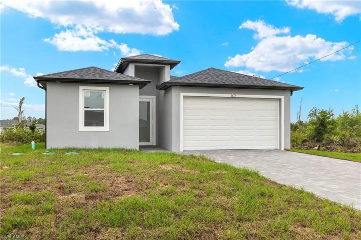 Prairie-style home with an attached garage, stucco siding, decorative driveway, and a front yard