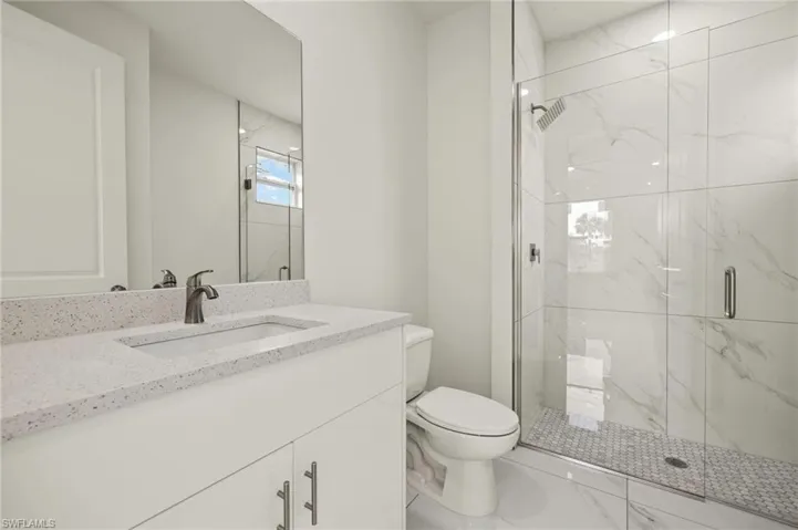 Full bath with toilet, a marble finish shower, vanity, and marble finish flooring