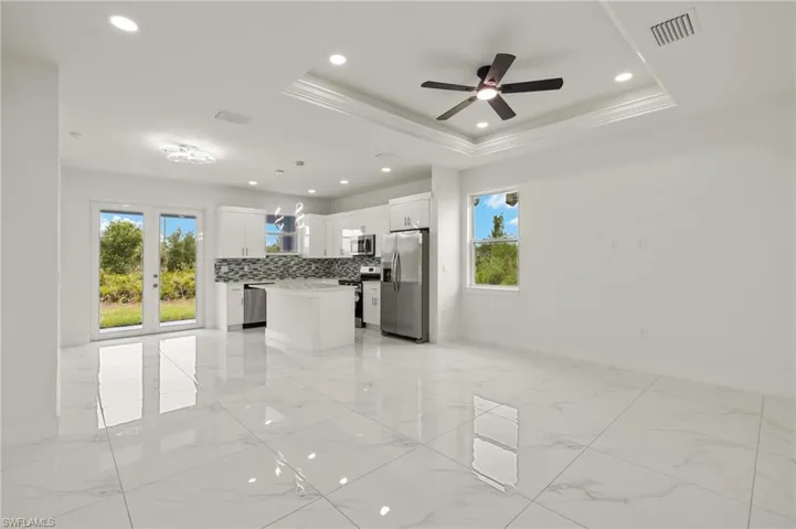 Unfurnished living room with healthy amount of natural light, baseboards, light marble finish flooring, ceiling fan, and recessed lighting