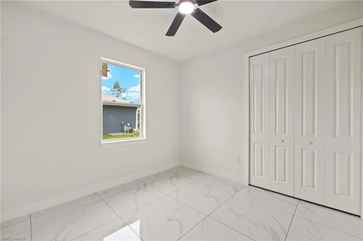 Unfurnished bedroom with light marble finish floors, baseboards, a closet, and ceiling fan